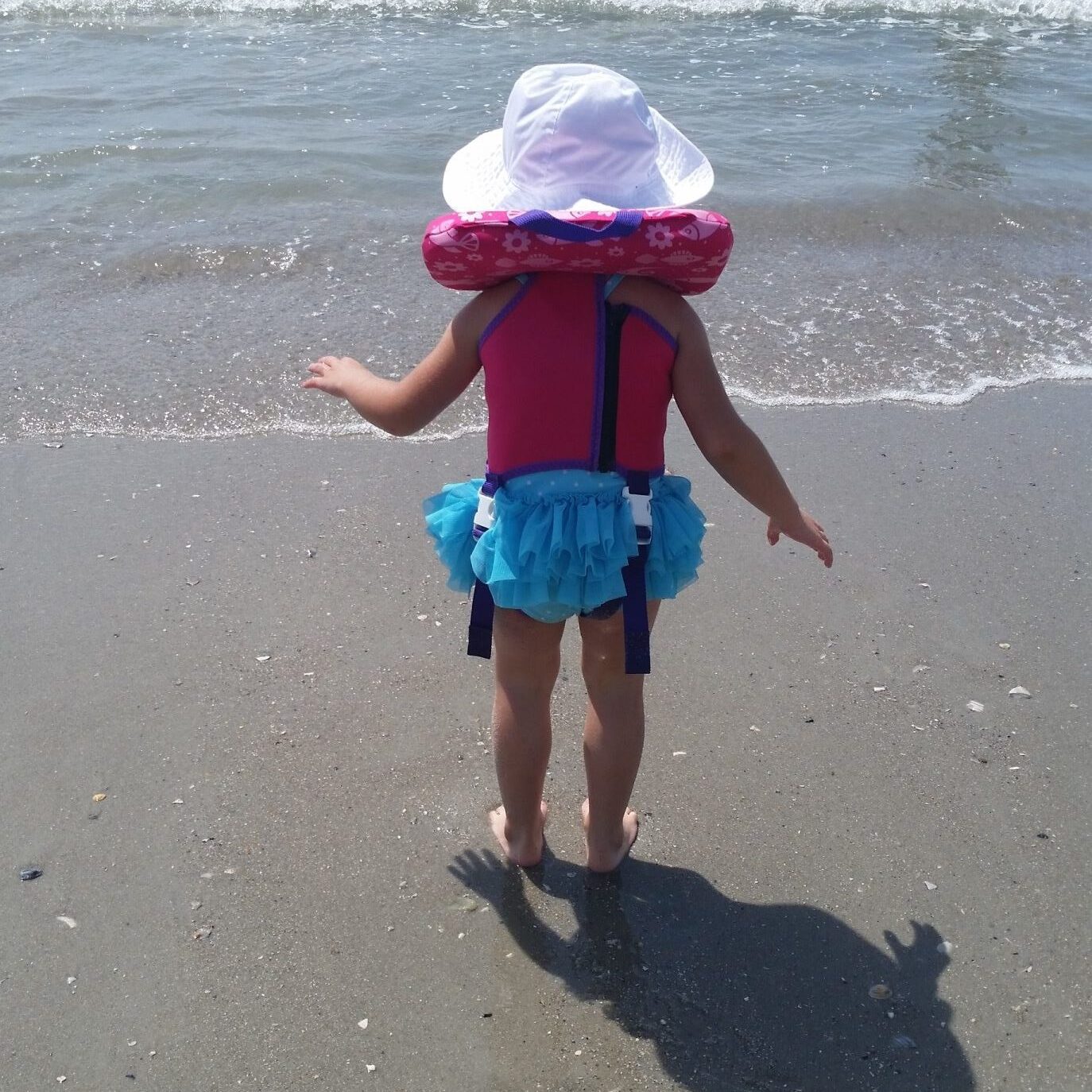 Child in personal floatation device watching incoming waves at the beach